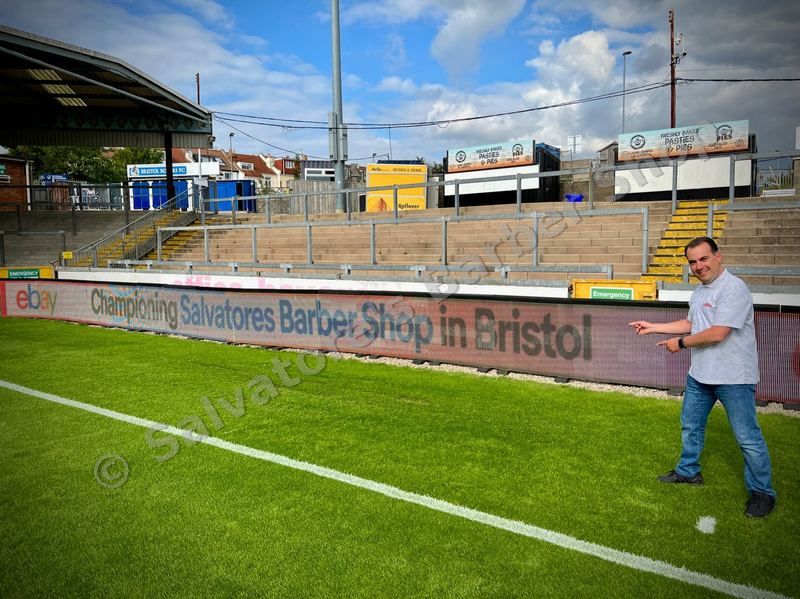 Salvatore next to eBay Championing Salvatores Barber Shop sign at Bristol Rovers